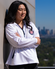 side view of female model leaning against wall with skyscrapers in background. she has her arms crisscrossed along her waist.