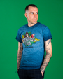 male model in frony of a green background. He is wearing the denim blue tee, black pants and has his hands in his pockets.