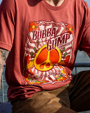 A close-up of a person wearing a rust-colored t-shirt featuring a vibrant "Bubba Gump Shrimp Co." design and peace symbol.