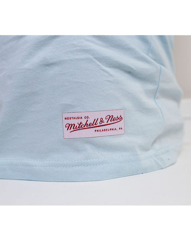 Close-up shot of the bottom hem of the same light blue short-sleeve tee with the "Mitchell & Ness" Label.