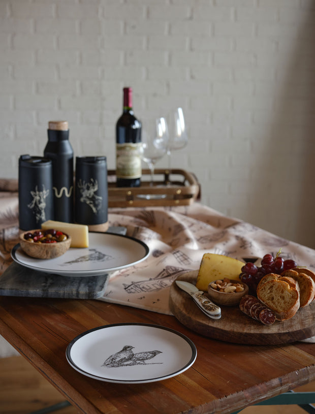 Dinner setting on wood table in front of white brick wall.