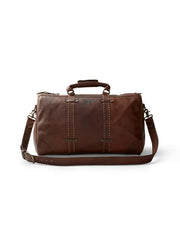 A brown leather weekender duffle bag with a textured finish is displayed against a white background. The bag features two rolled leather handles secured with stitching and metallic rivets, as well as a detachable, adjustable shoulder strap with metal clasps.  The front of the  duffle bag had the King Ranch symbol.